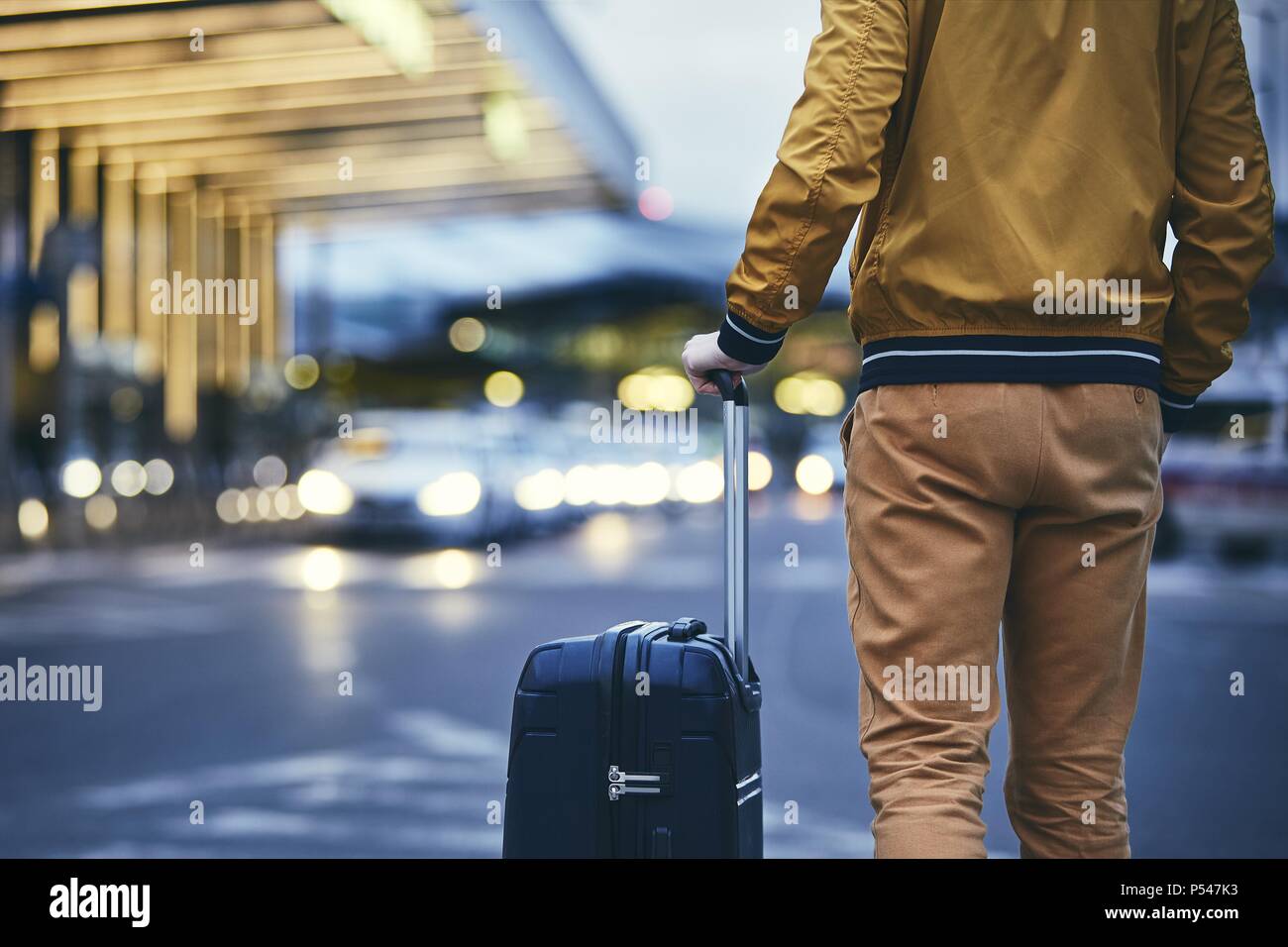 A piedi passeggero al di fuori del terminal dell'aeroporto. Vista posteriore del giovane uomo con i bagagli di notte. Foto Stock