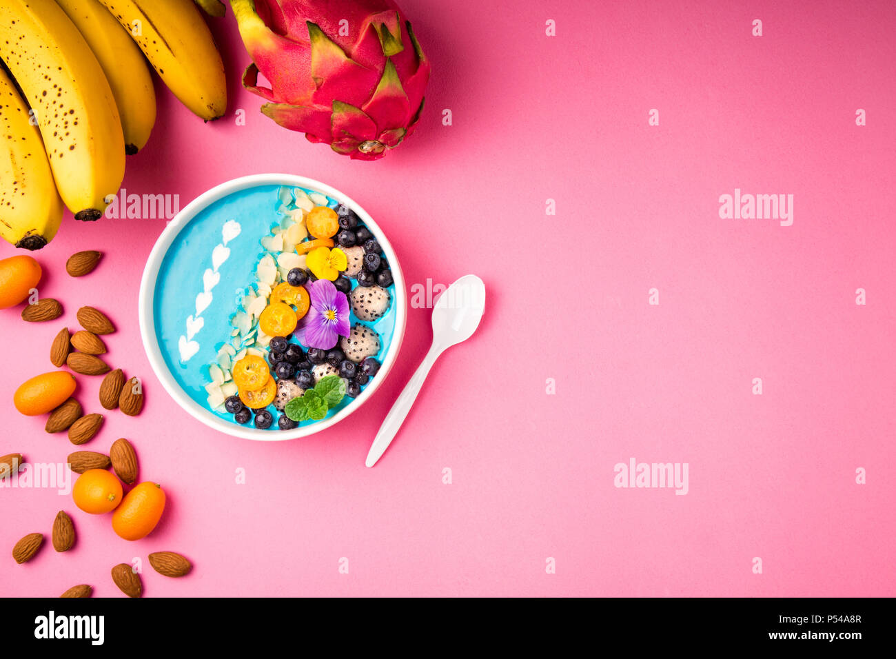 Ciotola frullato con frutti, bacche, dadi e fiori su sfondo rosa. Tropical frullato sano dessert. Una sana prima colazione, alimentazione vegetariana, lunch Foto Stock