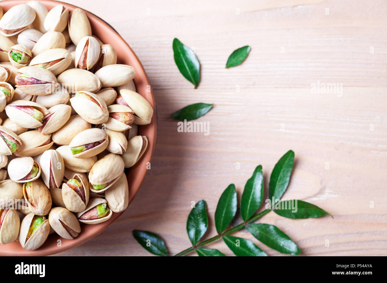 Pistacchi Noci in ciotola. Il pistacchio con foglie. Cibo sano, spuntini e cibo vegetariano. Vista superiore, spazio di copia Foto Stock