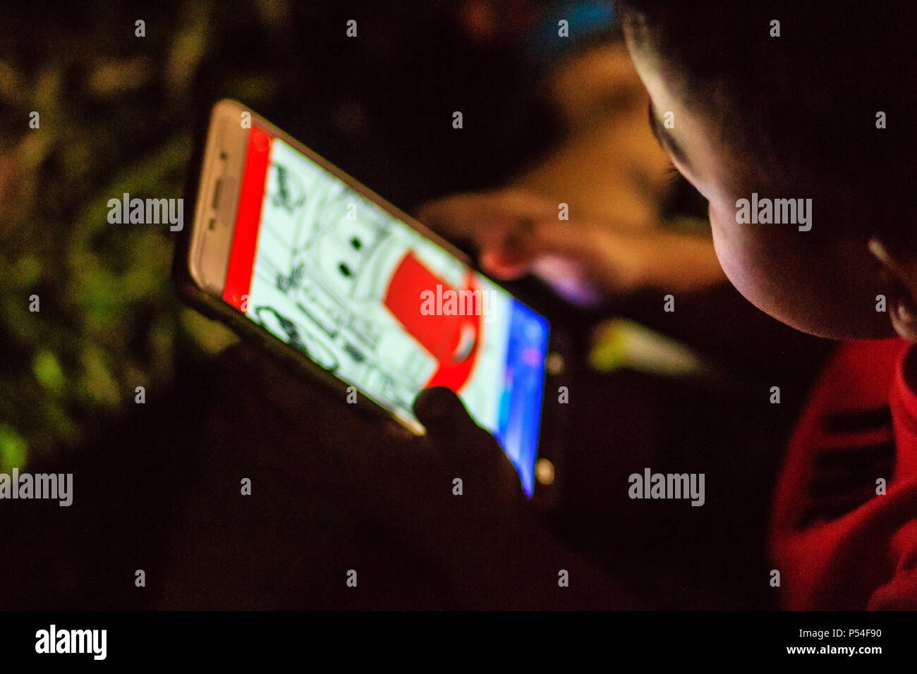 Ragazzo asiatico è concentrato a disegno con applicazione del telefono mobile nel buio della notte. Occhi il concetto di cura. Girato con ISO elevata con granella di rumore Foto Stock