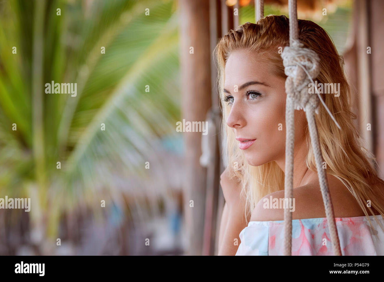 Giovane ragazza bionda seduta in una corda swing su una spiaggia caraibica Foto Stock