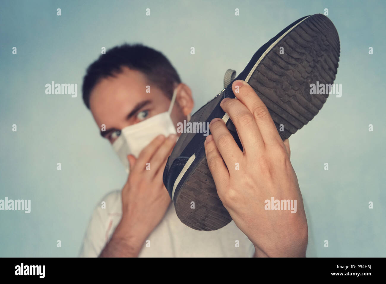 L'uomo con la maschera è azienda sporca puzzolente e cassoncino di pulizia - odore sgradevole concetto, sporca e puzzolente sneakers. Guarda le sneakers Foto Stock