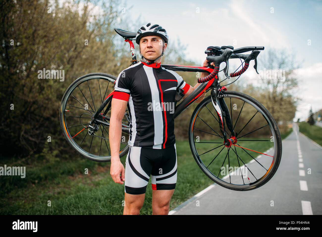 Bycyclist in casco e abbigliamento sportivo mantiene la bici sulla spalla  dopo ciclismo su strada asfaltata. Maschio sportivo corse in bicicletta.  Allenamento sul percorso per biciclette Foto stock - Alamy