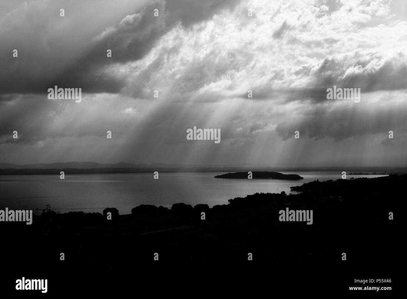 Raggi di sole che fuoriesce attraverso le nuvole sopra un isola in un lago Foto Stock