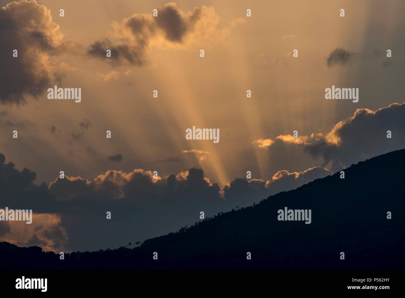 I raggi di luce filtra attraverso le nubi in un bel tramonto dietro la montagna Foto Stock