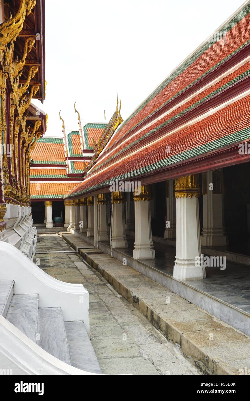 Vista lungo una passerella in pietra al palazzo imperiale di Bangkok con colonne abbinate e colorato tetto in piastrelle su un lato e. colonne dorate ornate all'altro Foto Stock