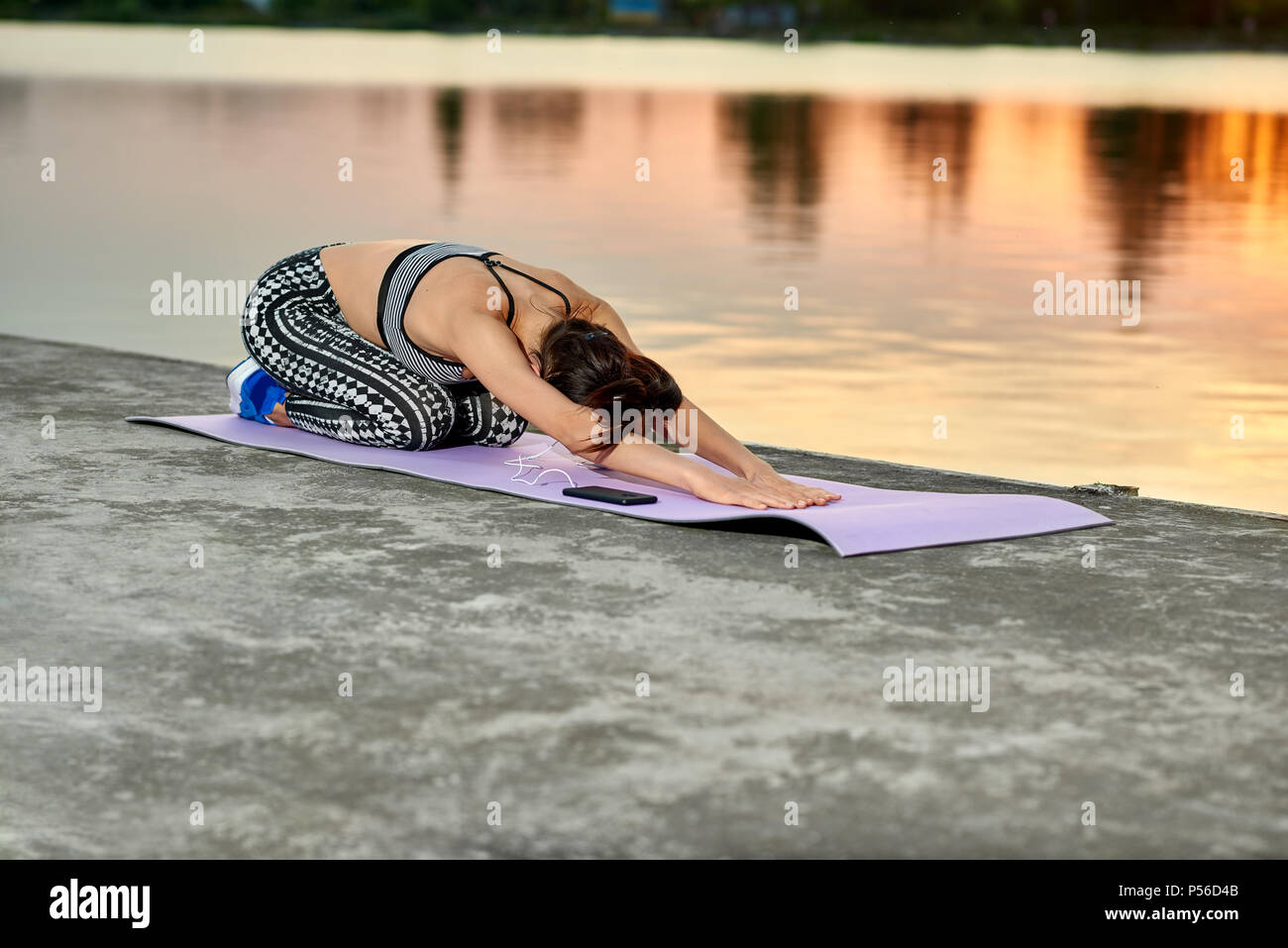 Montare la donna fare yoga pone vicino lago cittadino sul tramonto. All'esterno esercitando su aria fresca. Modello avente slim fit, bella figura. Il mantenimento di uno stile di vita sano. Sport, yoga e fitness. Foto Stock