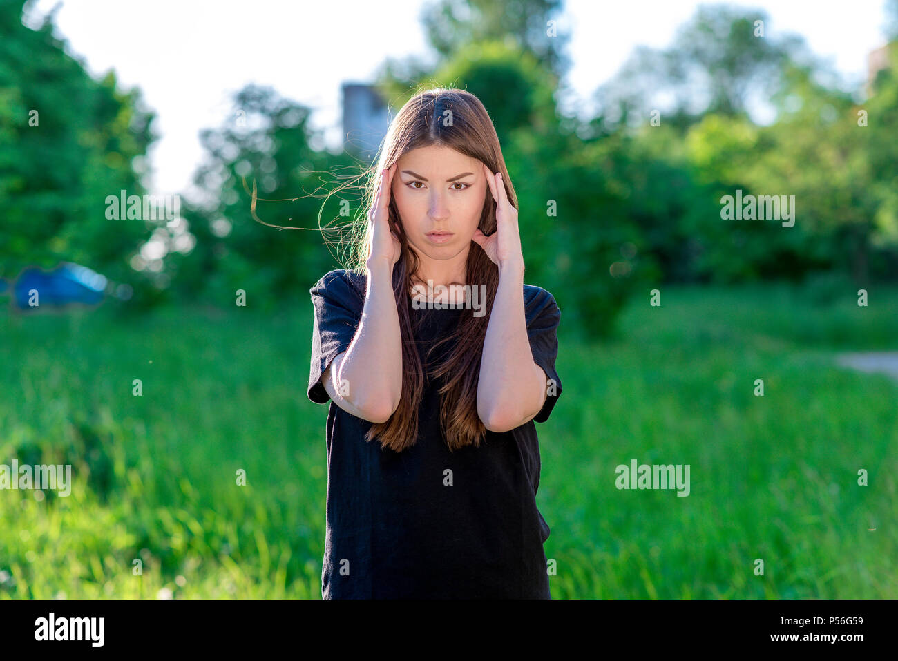Una bruna donna è asiatica. Tiene le mani vicino alla testa. Le emozioni sono un forte mal di testa di emicrania. In estate nel parco all'aria fresca. Foto Stock