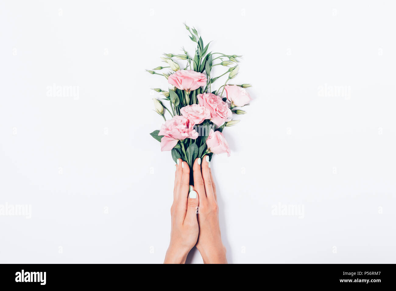 Donna con le mani alla moda di manicure holding mazzetto di fiori di colore rosa su sfondo bianco, vista dall'alto. Piano di composizione laici fioraio rendendo un bouquet di bellezza Foto Stock