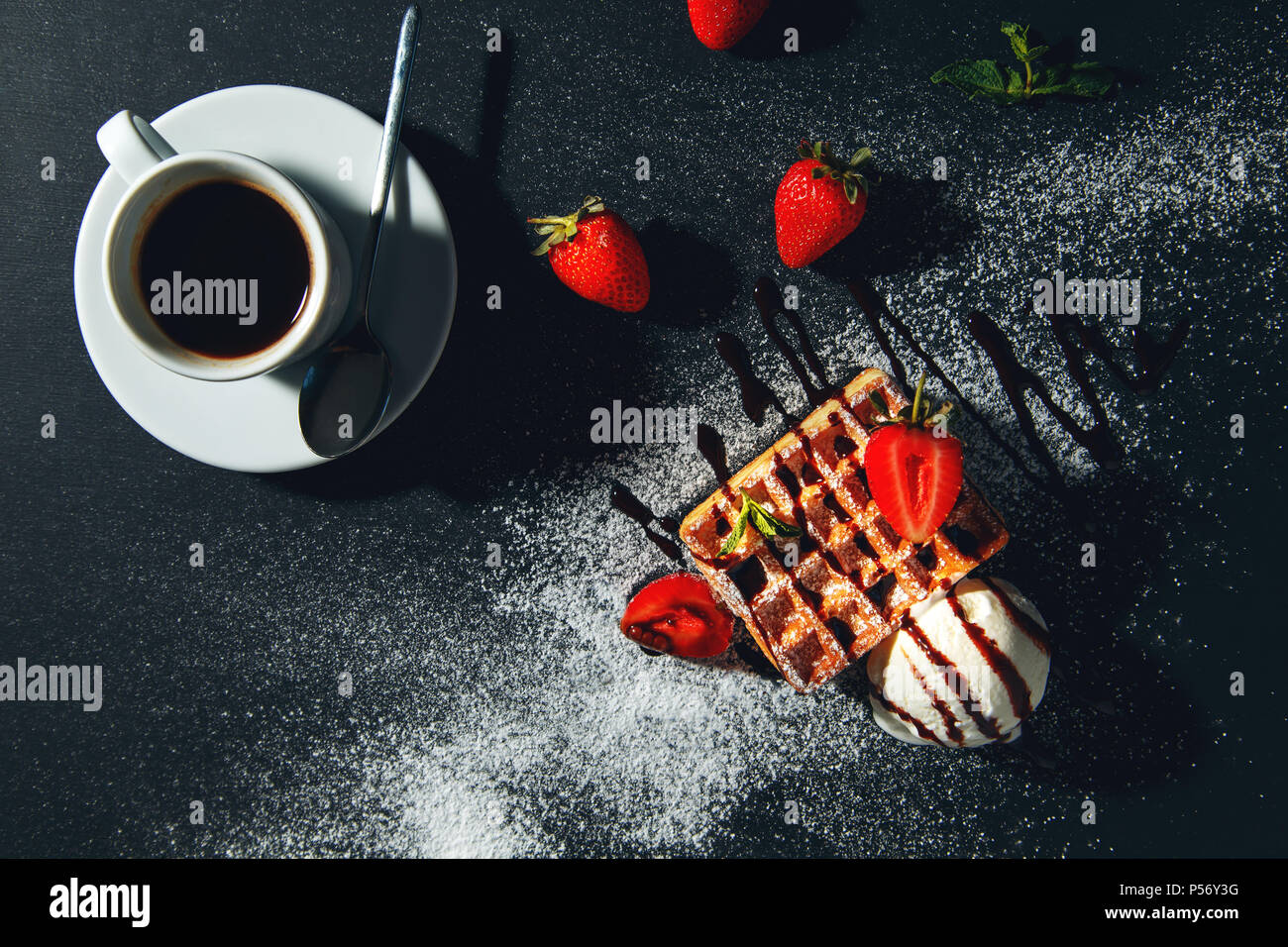 Tazza di caffè con cialde belghe con gelato e fragole su uno sfondo nero. Foto Stock