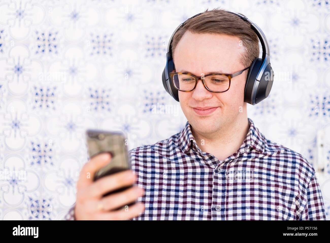 Giovane Uomo con cuffie bluetooth collegato allo smartphone in mano Foto Stock