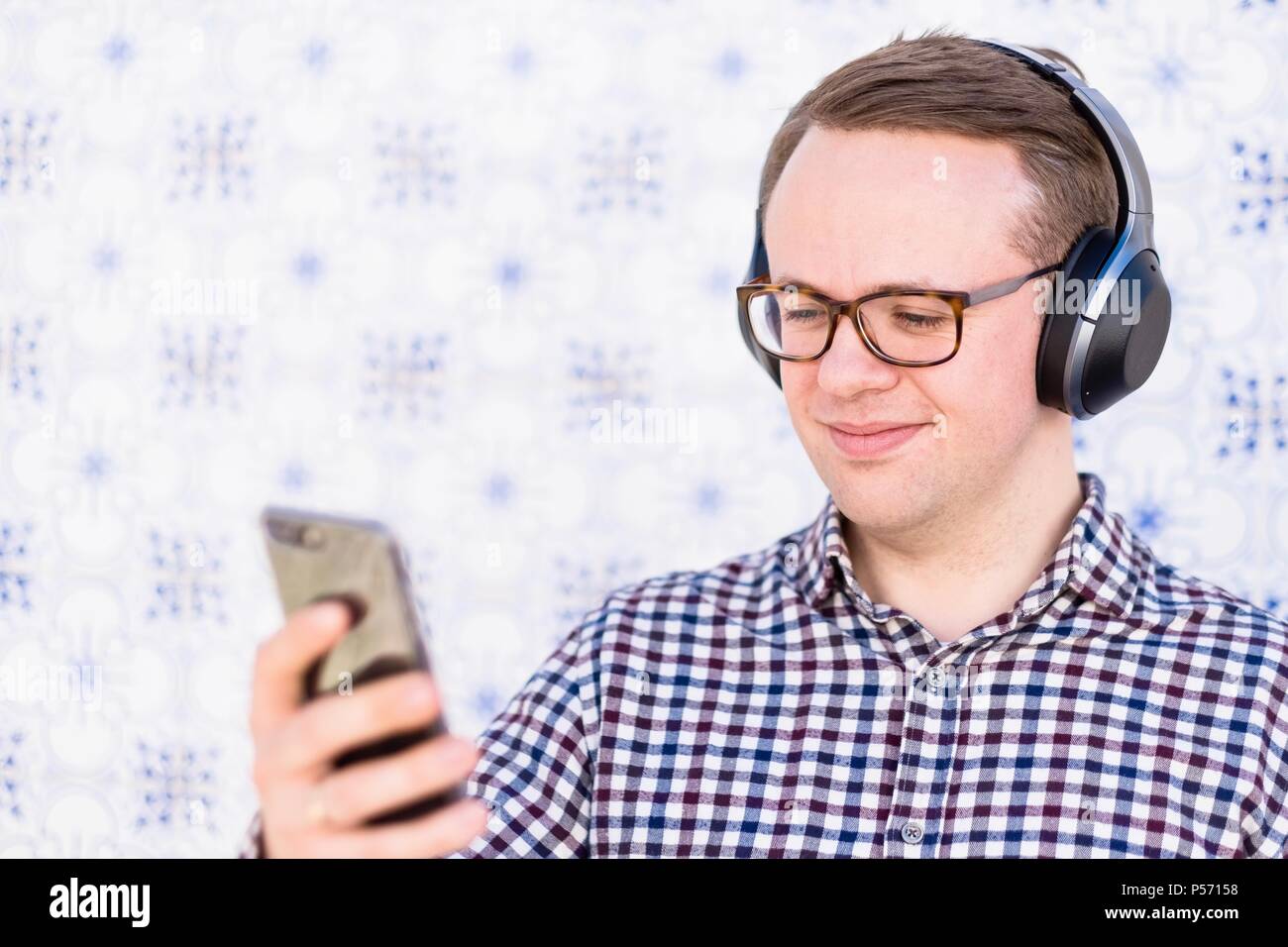 Giovane Uomo con cuffie bluetooth collegato allo smartphone in mano Foto Stock