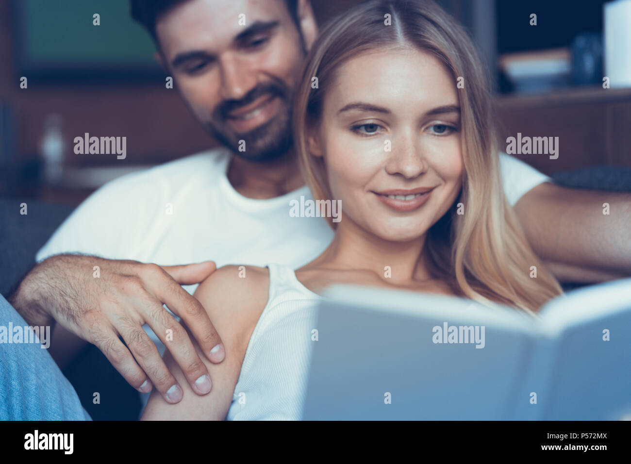 Trascorrere del tempo piacevole a casa. Giovane e bella coppia amorevole legame ad ogni altro e sorridere mentre la donna in possesso di un libro Foto Stock