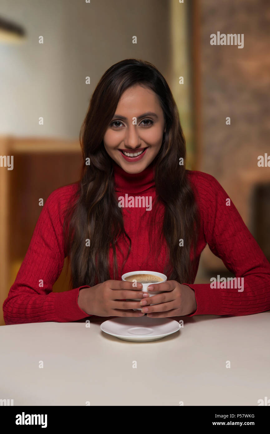Sorridente giovane donna con tazza di caffè guardando la fotocamera Foto Stock