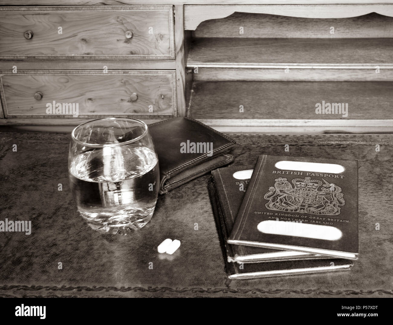 Blu passaporto britannico con custodia in cuoio, vetro di acqua e pillole su legni antichi scrivania in seppia Foto Stock
