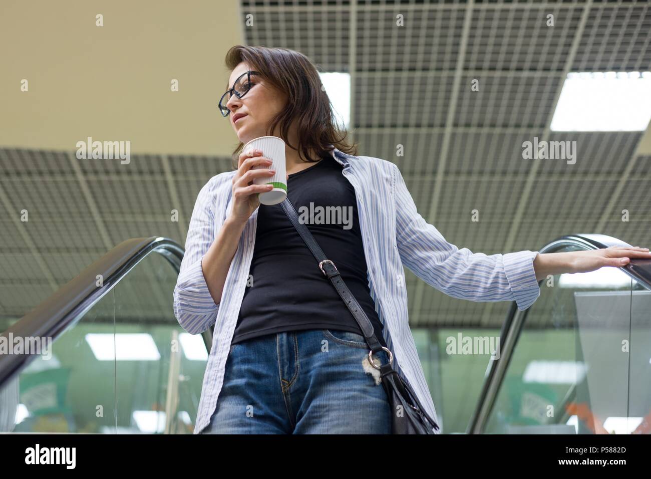 Donna di mezza età con tazza di caffè, sfondo shopping mall un centro di intrattenimento. Stile di vita, il tempo libero e il concetto di popolo. Foto Stock