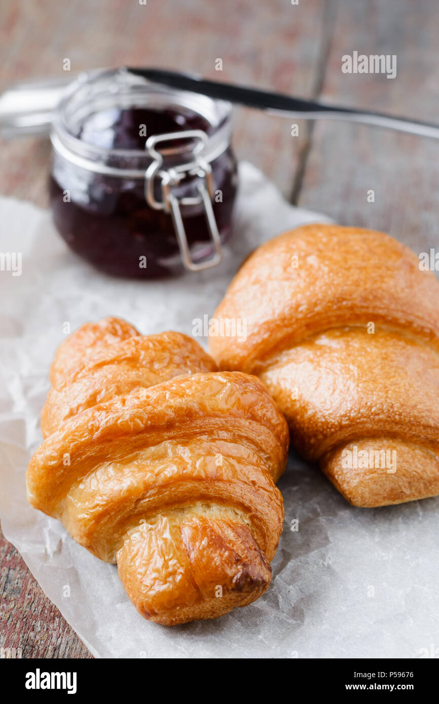 Due croissant e un vasetto di marmellata su un sfondo di legno. Prima colazione francese Foto Stock
