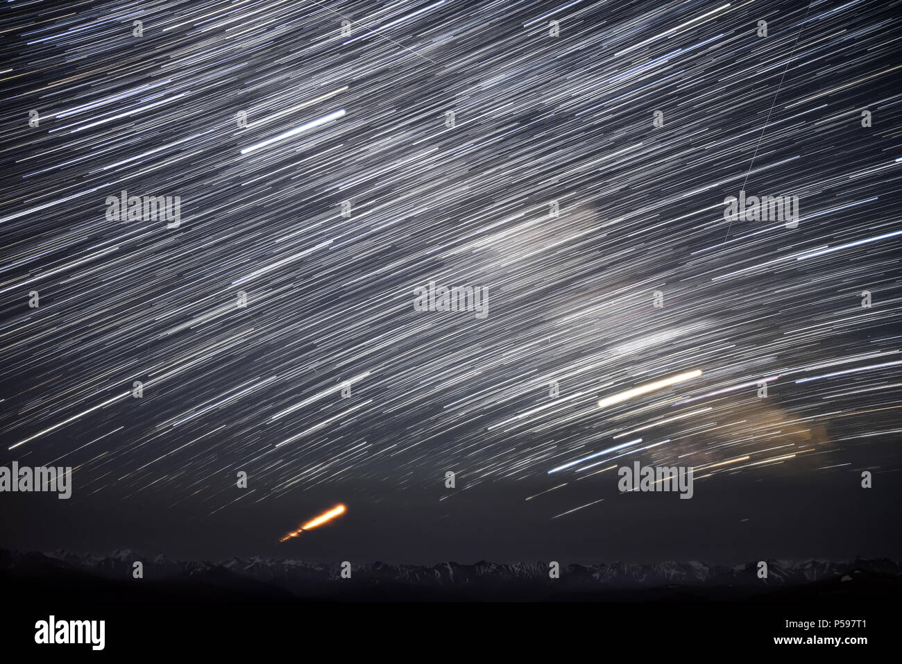 Un bellissimo panorama notturno del cielo stellato con tracce di meteore e stelle nella forma di piste circolari contro lo sfondo del Monte Nevoso Foto Stock