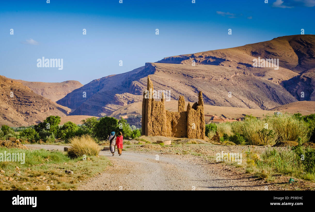 Due donne berbere camminano davanti a una Kasbah in rovina nella Gola di M'Goun nel Marocco meridionale Foto Stock