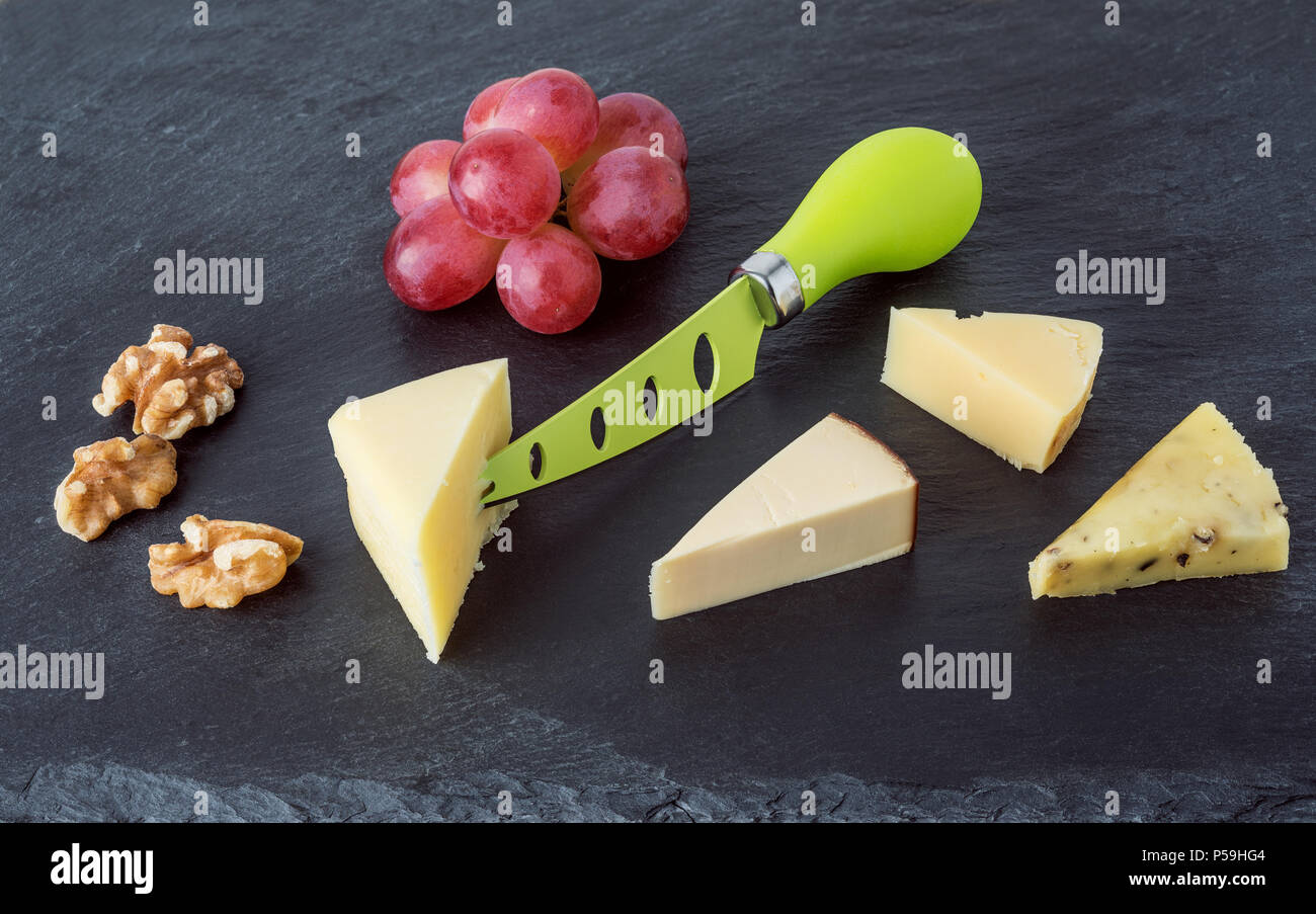 Vassoio di formaggi formaggi diversi con uve e mallo di noce nera sulla piastra di ardesia.vista superiore Foto Stock