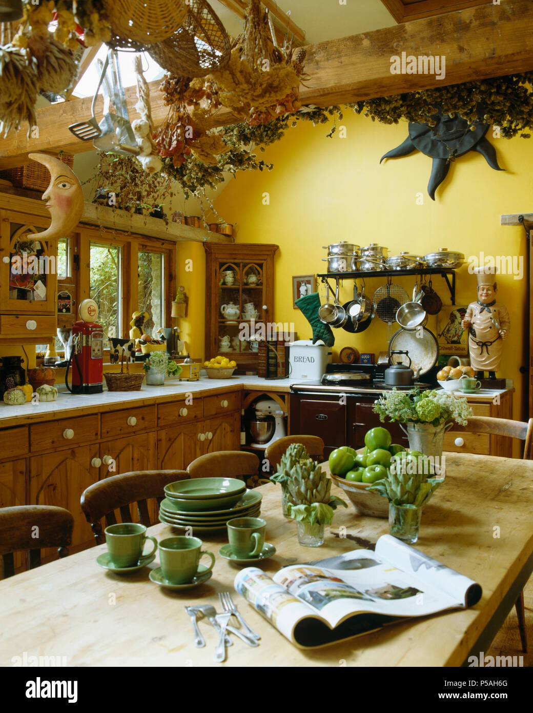 Verde pallido piatti sul tavolo di legno in colore giallo tradizionale cucina di paese con secchi floers pendenti dal soffitto travi Foto Stock
