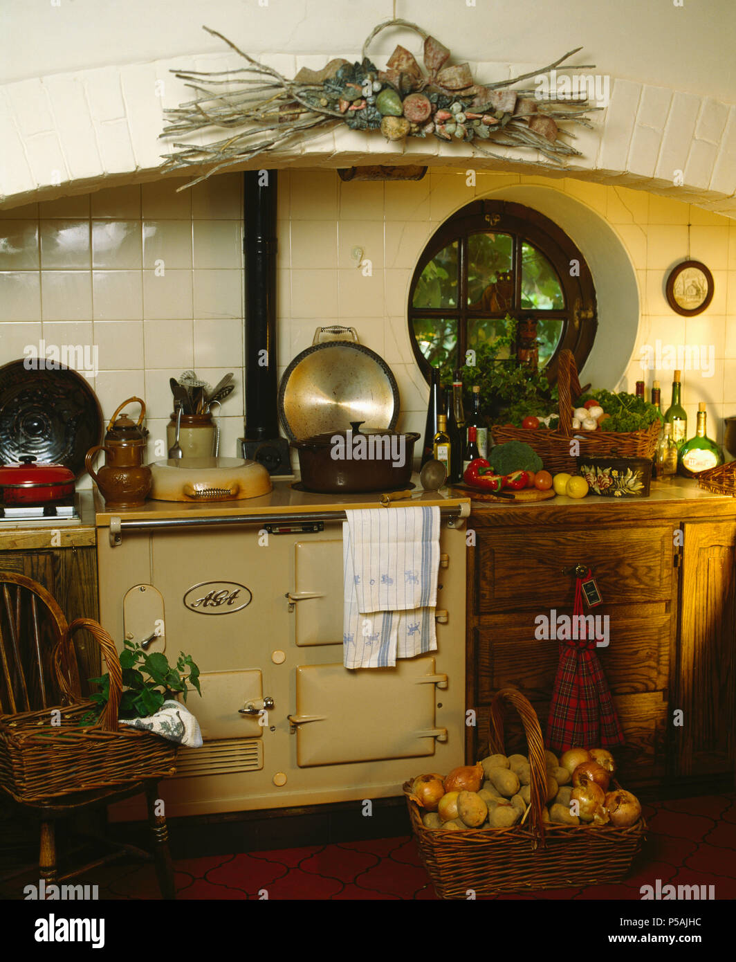 Cesto di cipolle e patate nella parte anteriore della crema Aga in cottage cucina con finestra circolare Foto Stock