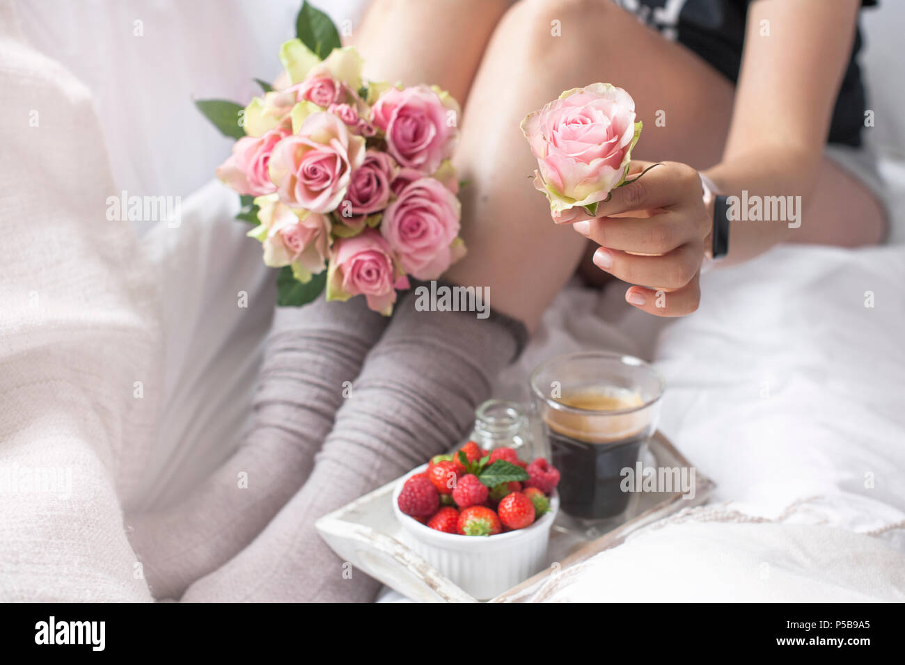 Un bouquet di rose rosa nelle mani della ragazza sul letto, bacche di fragole e un fragrante caffè del mattino. Il Romance. Foto d'epoca. Spazio di copia Foto Stock