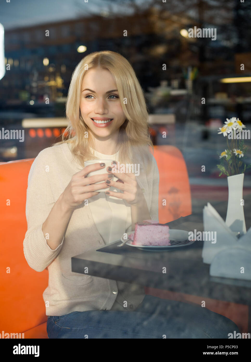 Molto bella e felice, giovane donna, sedersi al bar e bere un tè o un caffè con croissant, street la visuale della finestra frontale Foto Stock