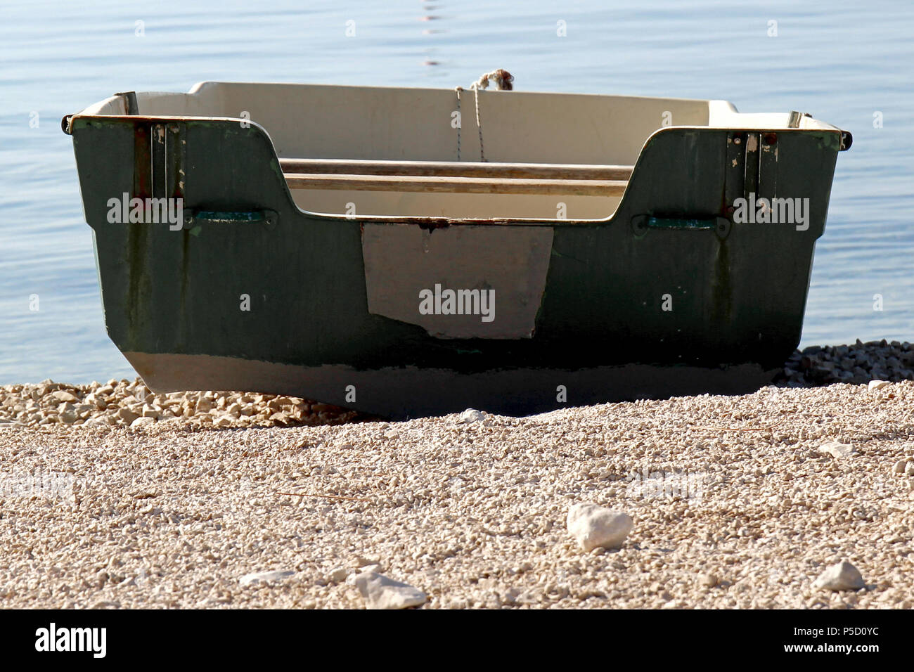 Ein leeres Boot in grün weiß von hinten an einem Kiesstrand. Foto Stock