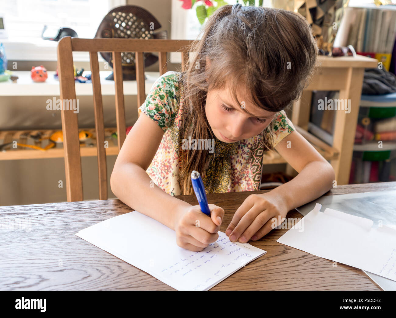 Una ragazza scrive i suoi compiti a casa su un foglio bianco di carta con una penna a sfera Foto Stock