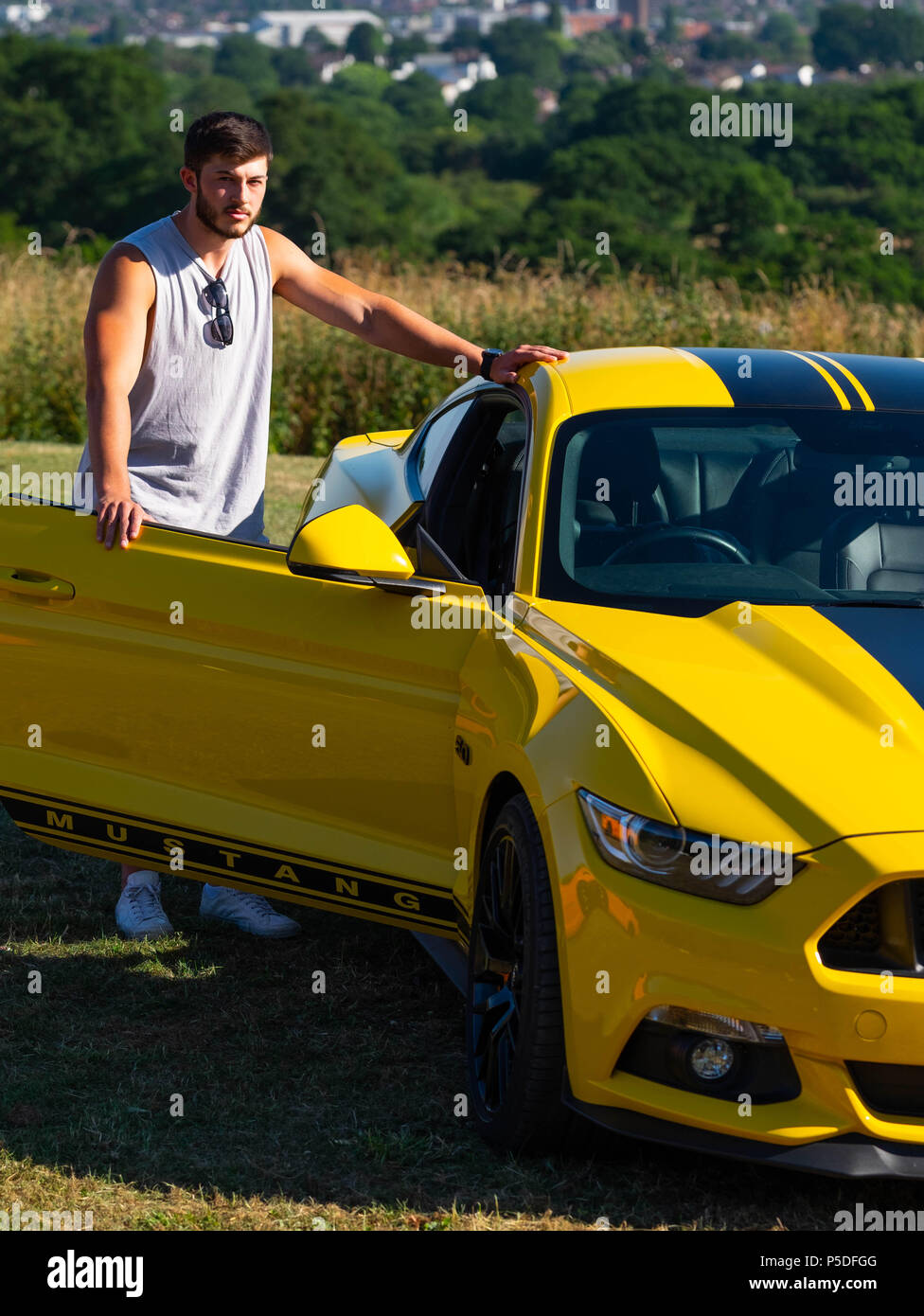 Muscolare di giovane uomo pone con un europeo Ford Mustang 5 litri V8 GT Fastback Auto Auto sportiva nel Regno Unito Foto Stock