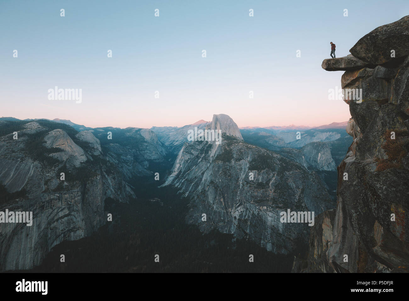 Un intrepido escursionista è in piedi su una roccia a strapiombo godendo della vista verso il famoso Half Dome presso il Glacier Point si affacciano nella splendida post tramonto twil Foto Stock