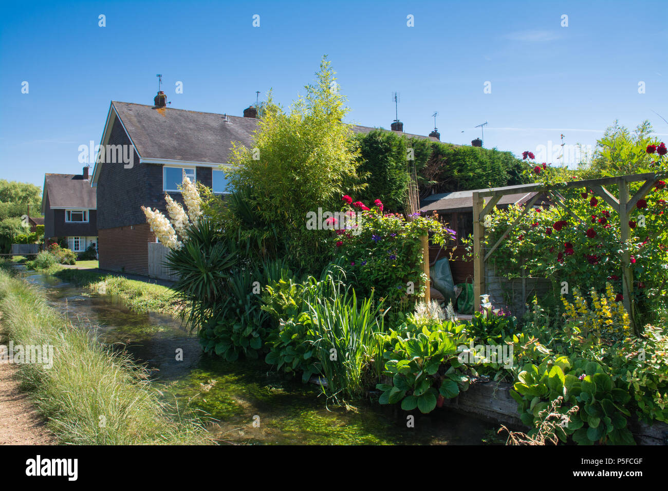 Case e giardini su una soleggiata giornata estiva a fianco di un ramo del fiume Test in Stockbridge, Hampshire, Regno Unito Foto Stock