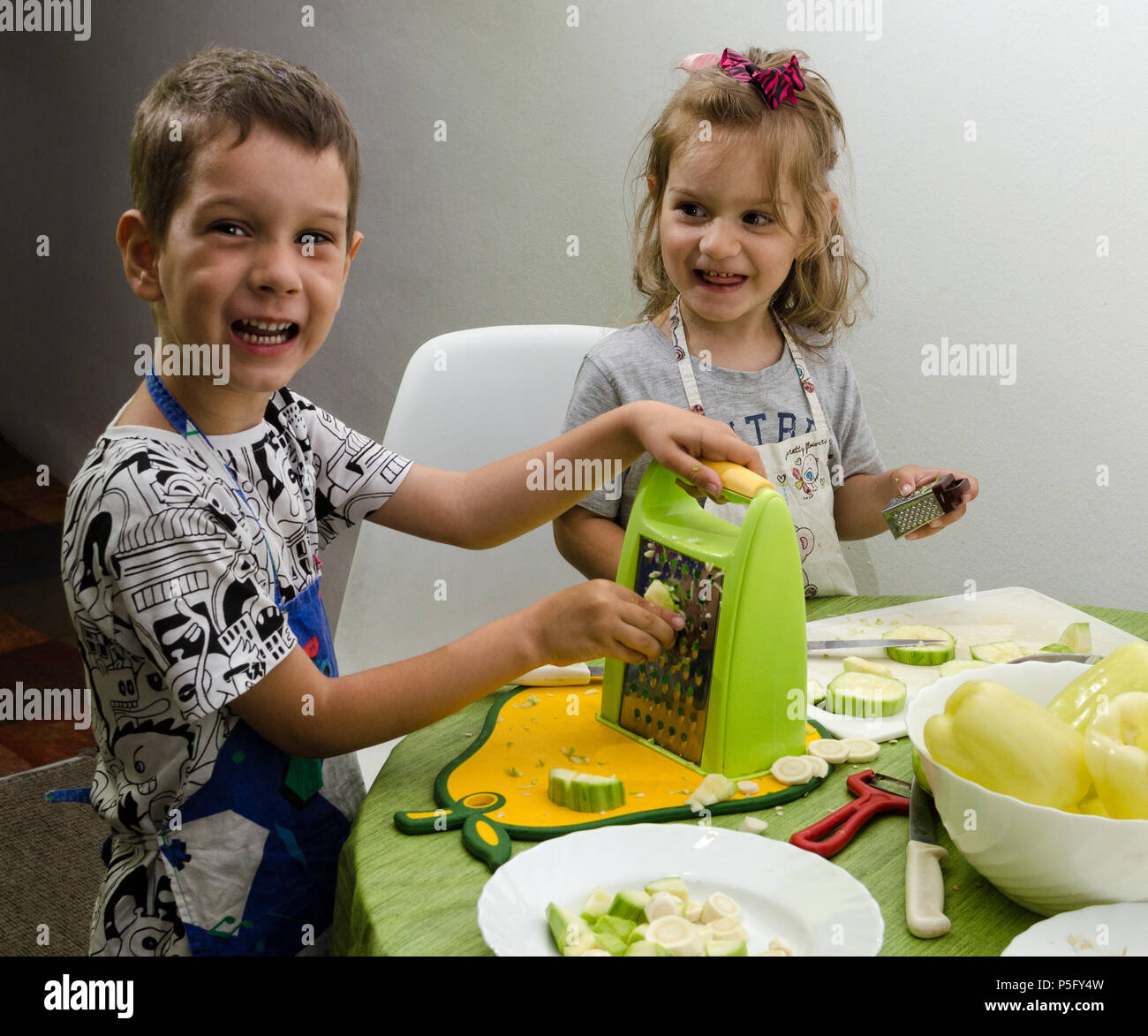 Due bambini piccoli, di due e quattro anni di aiutare a preparare il cibo per il pasto successivo dalla macinazione di zucchine e paprika. Foto Stock