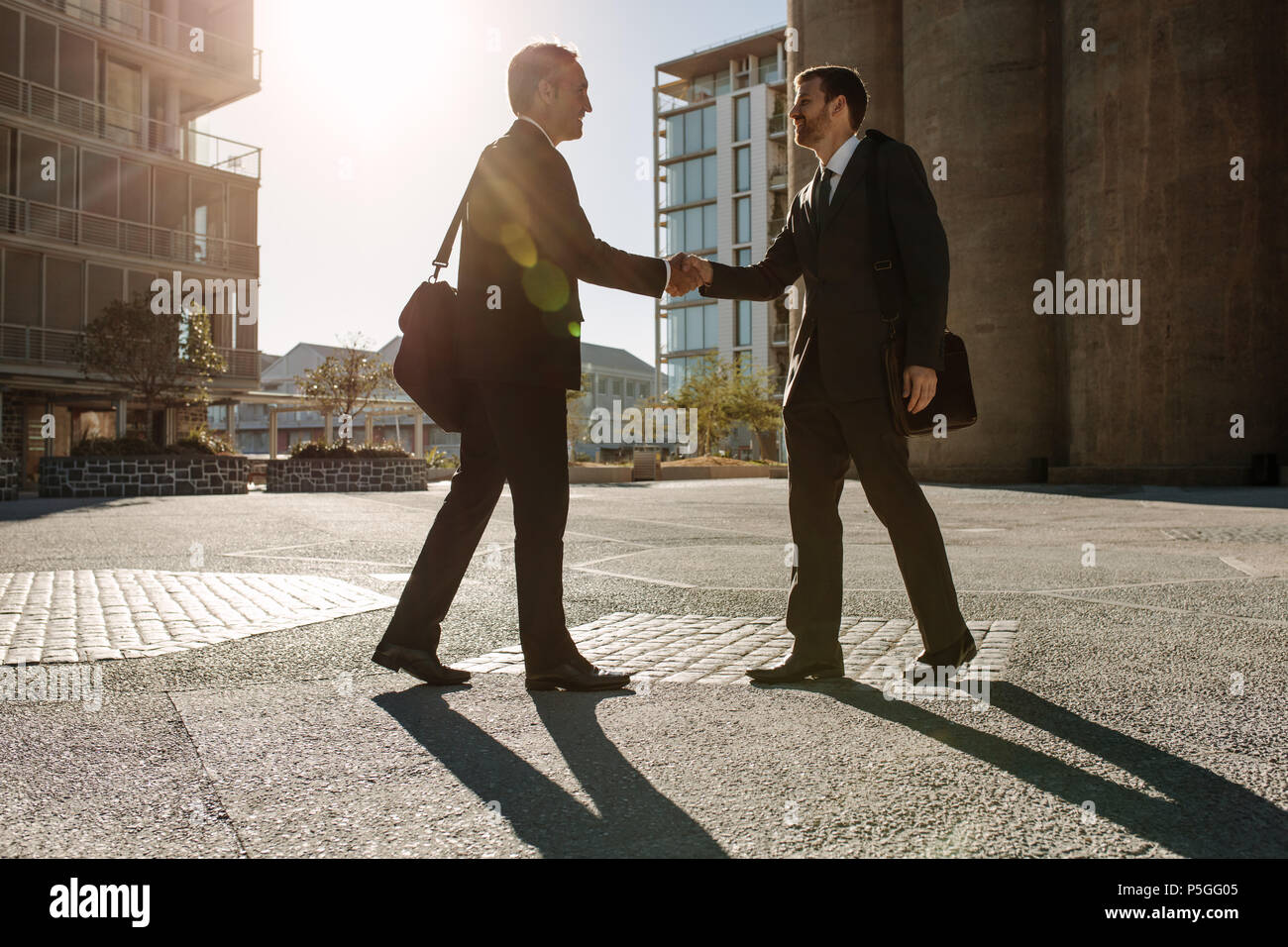 Colleghi di lavoro che saluto ciascuno di loro e scuotimenti mani su una strada mentre il pendolarismo per ufficio. Vista laterale di imprenditore agitando la mano con un colleag Foto Stock