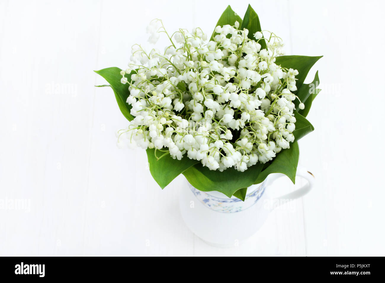 Bel bouquet di mughetti in Caraffa del Bianco su bianco verniciato tavolo in legno Foto Stock