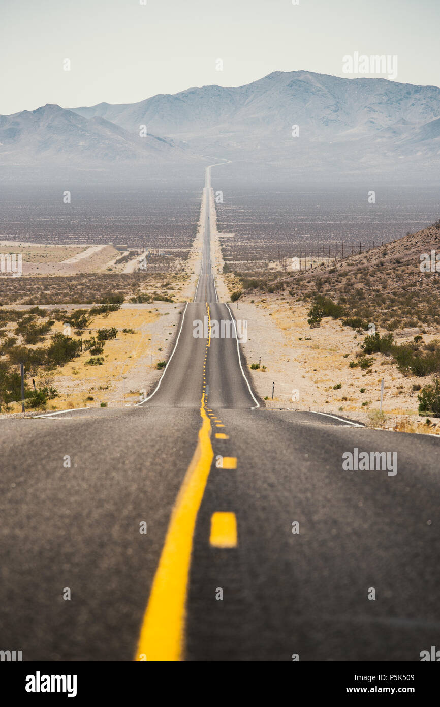 Classic vista panorama di un interminabile dritta strada che corre attraverso il paesaggio arido del sud-ovest americano con estremo calore opacità su un bellissimo s Foto Stock