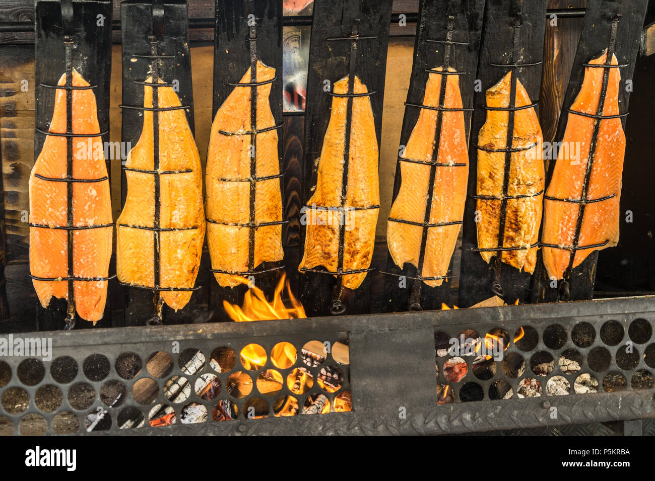 Preparazione del salmone di fiamma su aprire il fuoco di un caminetto aperto caricato con legno, Germania Foto Stock