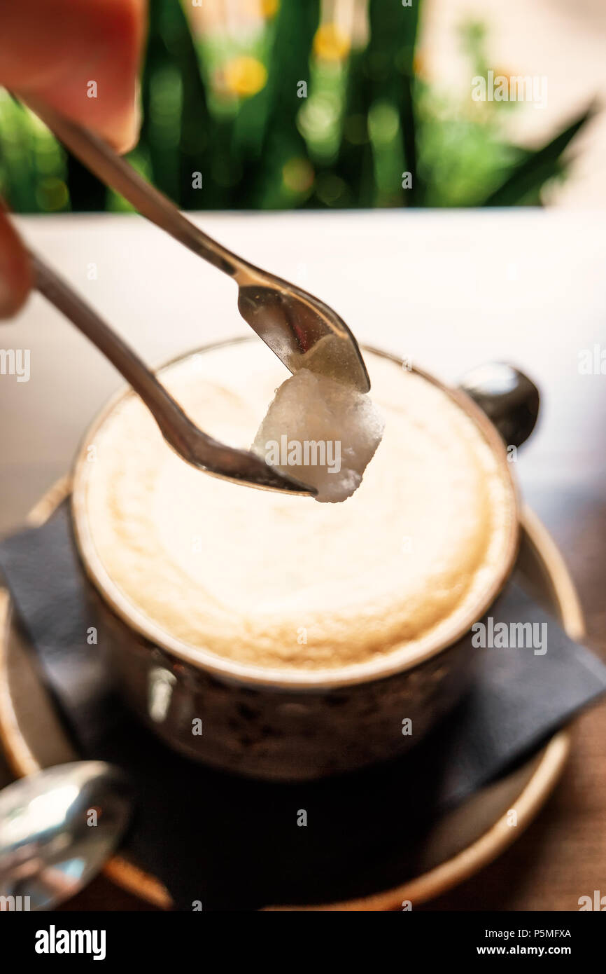 Aggiungere lo zucchero nella tazza di latte caldo il caffè sul tavolo in legno Foto Stock