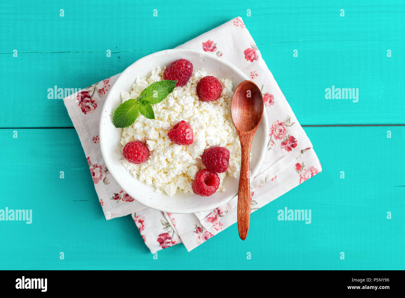 Ricotta con lamponi in una ciotola di legno color turchese sfondo. Ricotta, formaggio tvorog,. Mangiare sano, uno stile di vita sano, estate dess Foto Stock