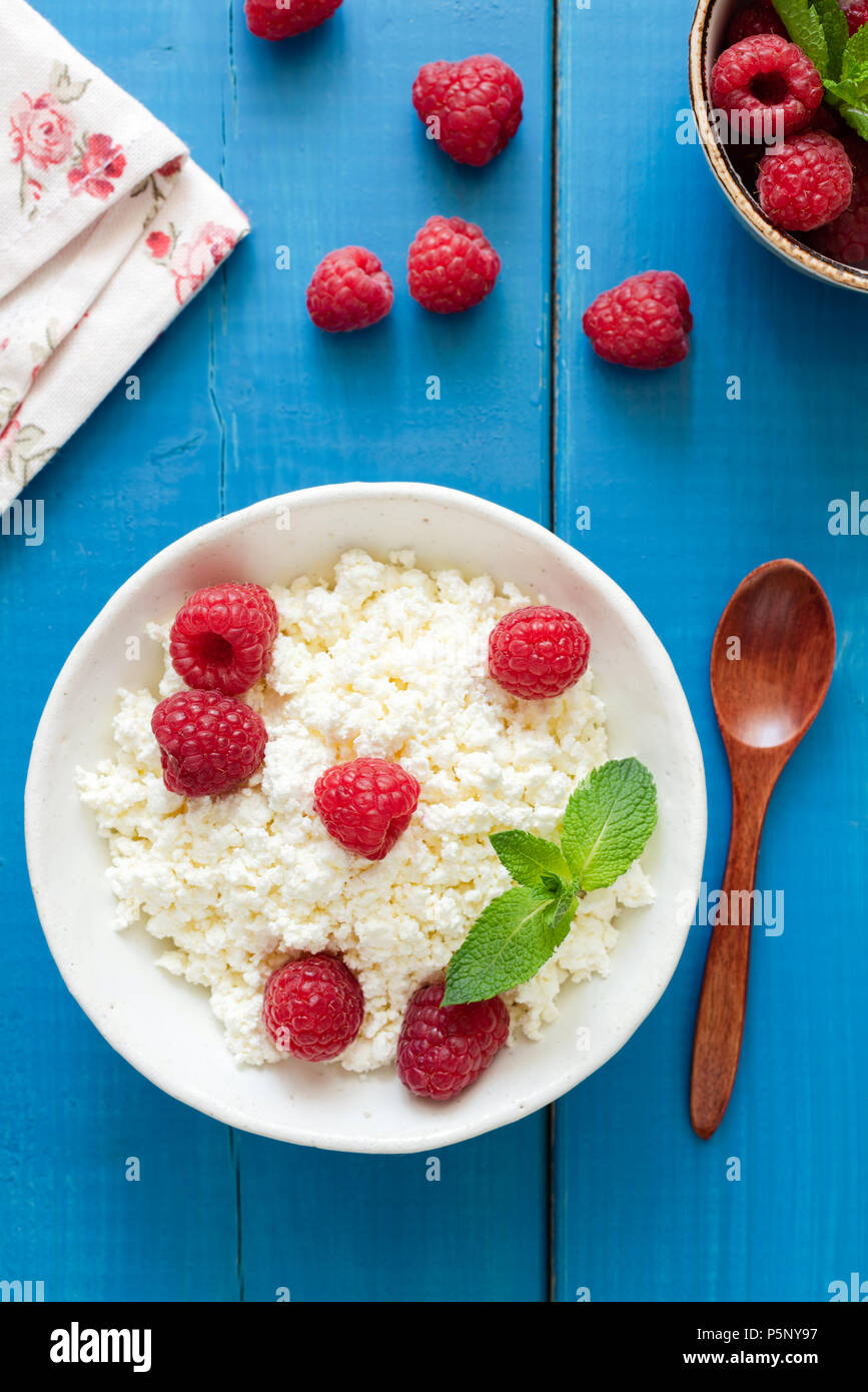 Ricotta con lamponi in una ciotola di legno blu sullo sfondo. Ricotta, formaggio tvorog,. Mangiare sano, uno stile di vita sano, dessert estivo o Foto Stock