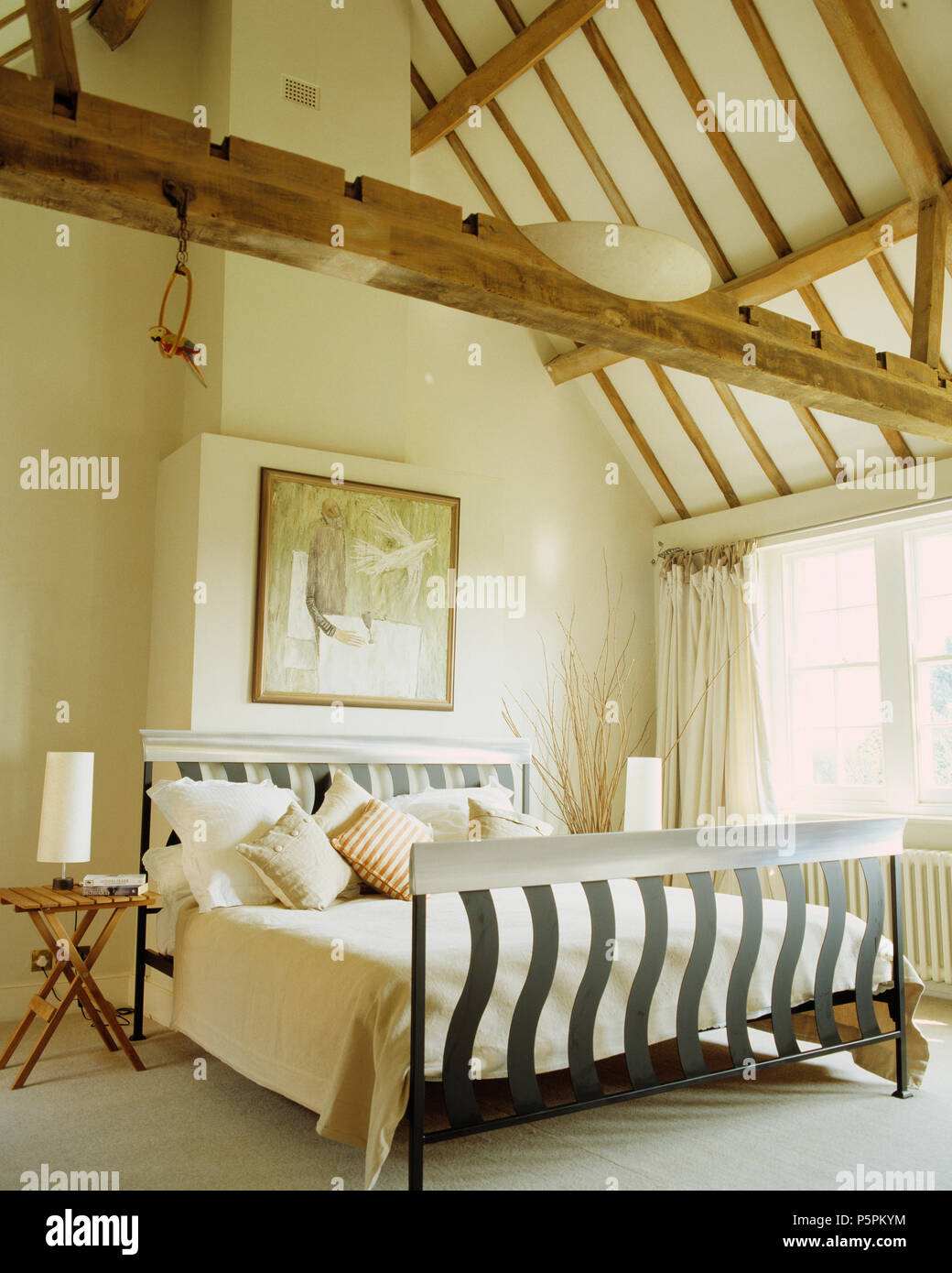 Moderno letto in metallo con crema di trapunte e cuscini in crema di conversione del granaio camera da letto con travi a soffitto apex Foto Stock