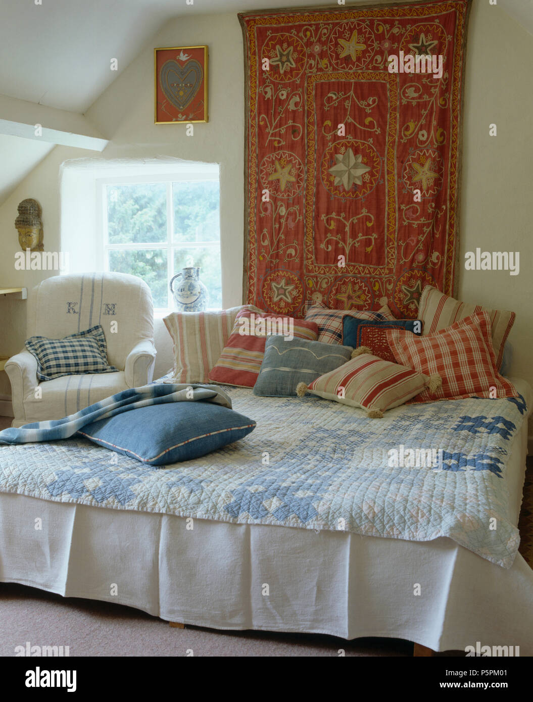 Paese camera da letto in stile indiano wall-appeso sopra il letto con impilati a strisce rosse e verifica dei cuscini e un blu mosaico Foto Stock