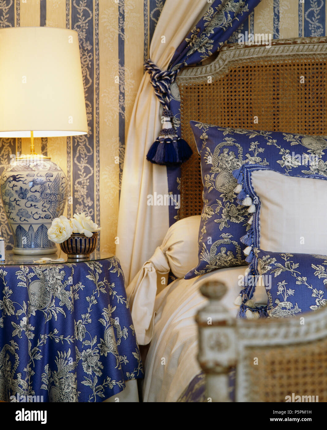 Close-up di ghted lampada sul tavolo con blue+bianco panno floreali accanto all antico letto Bergere con blue+bianco cuscini floreali Foto Stock