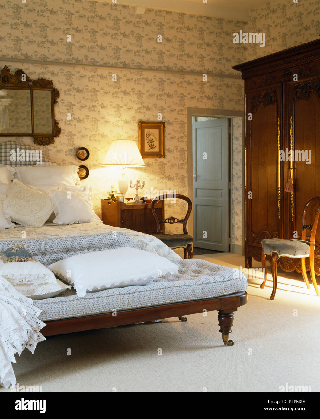 Blu pallido divano ai piedi del letto con lenzuola bianche nel paese francese camera con Toile de Jouy wallpaper Foto Stock