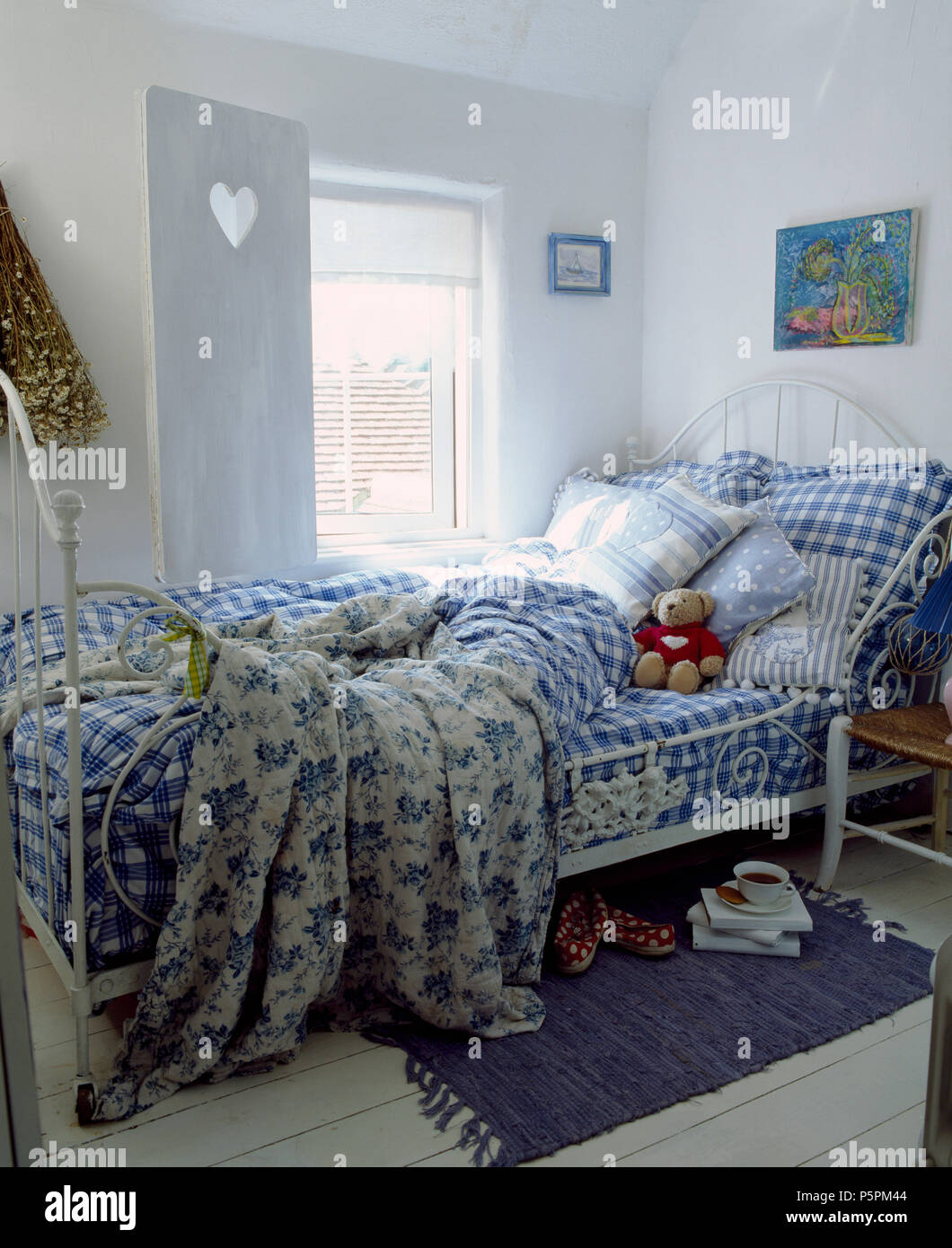 Blue+bianco a scacchi biancheria da letto e piumini floreali su bianco ferro battuto letto matrimoniale in camera da letto del paese con persiane bianche Foto Stock