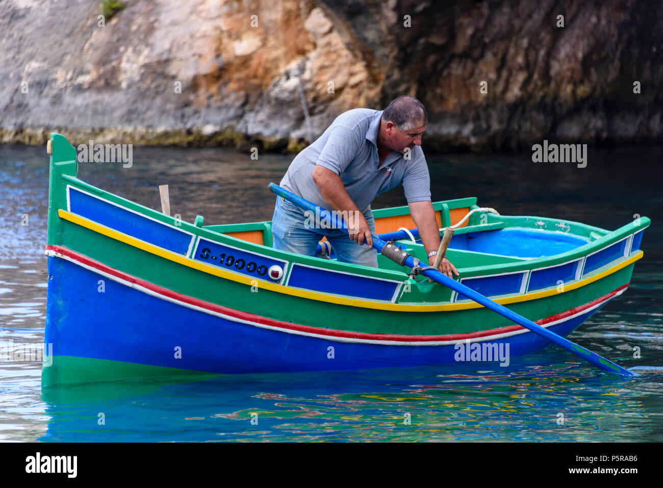 Un pescatore di righe il suo tradizionale maltese barca a remi nella baia di Xlendi a raccogliere le gabbie di aragosta. Foto Stock