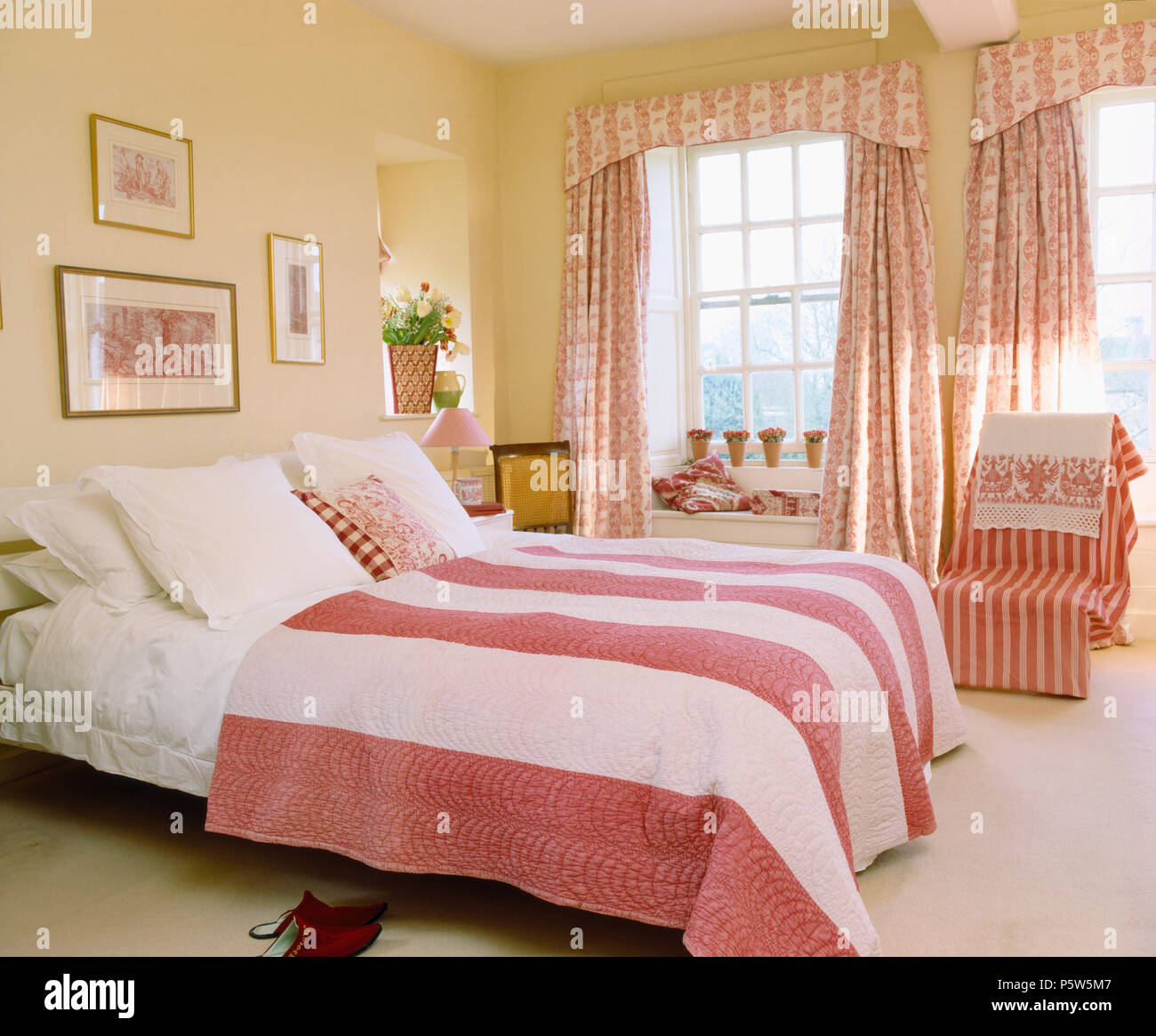 Rosa+white wide-quilt striato sul letto con cuscini bianchi nel paese camera da letto con il rosa+bianco tende floreali su windows Foto Stock