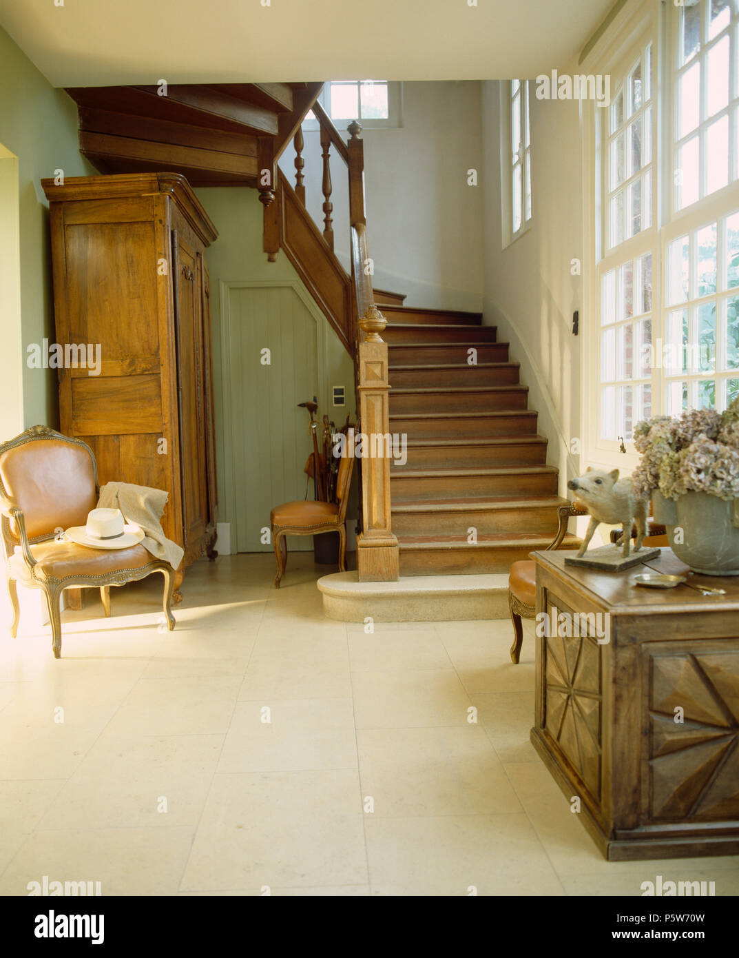 Sedia antica e mobilia di legno scolpito petto nel paese francese sala con pavimento piastrellato in pietra e la scalinata in legno di quercia Foto Stock