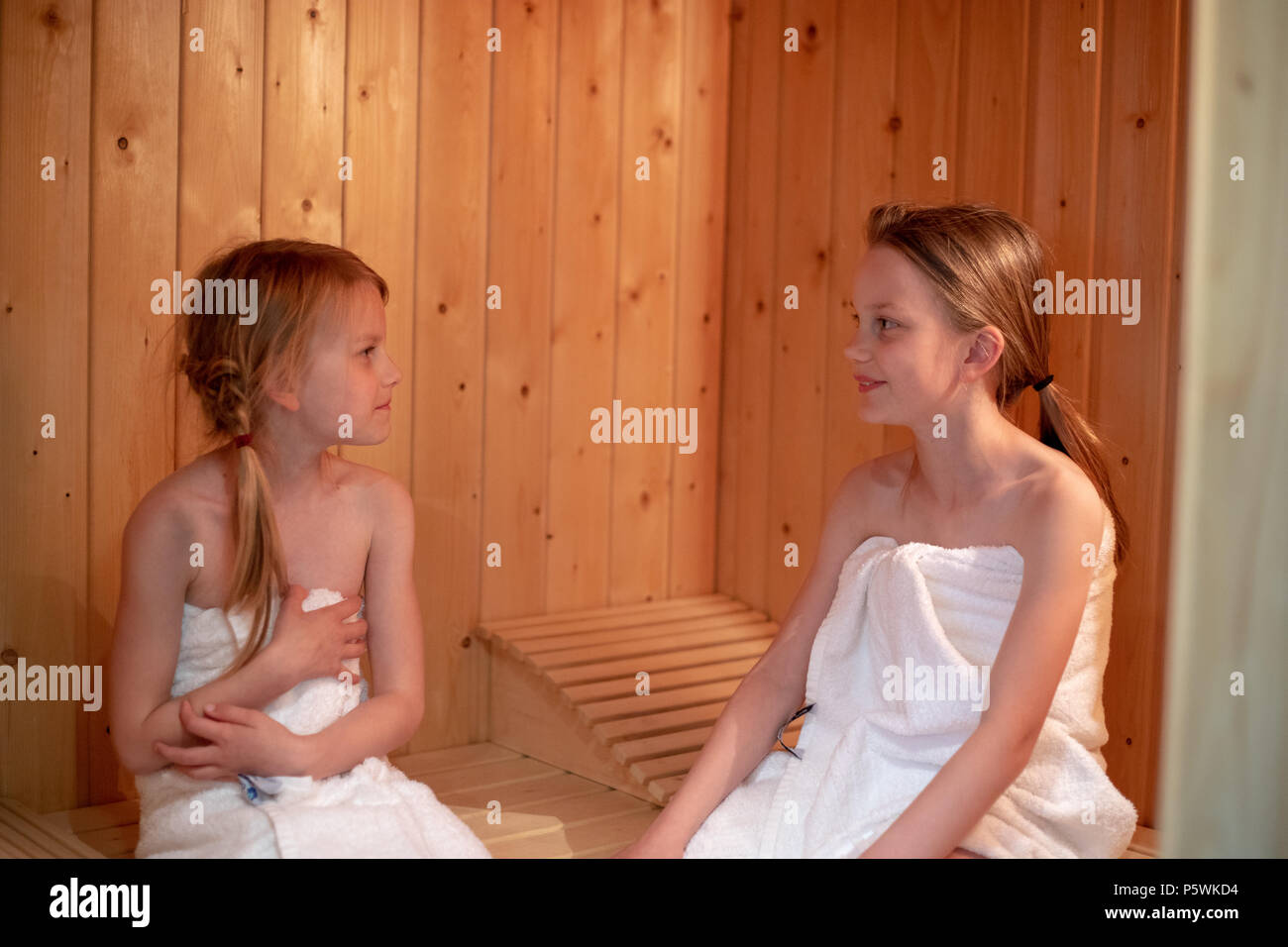 Due ragazze hanno essi stessi avvolti in asciugamani e sono seduti in una sauna finlandese Foto Stock